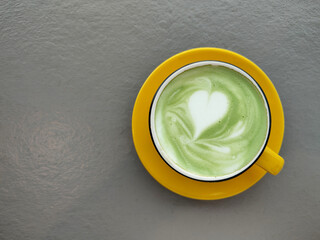 Hot green tea with heart shape latte art in yellow cup on grey background