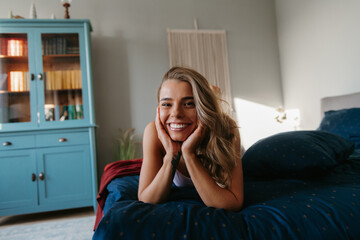 Relaxed young woman lying in bed and smiling while spending carefree time at home