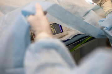 An anesthesiologist's hand near a monitor with the patient's vital signs during surgery. The...