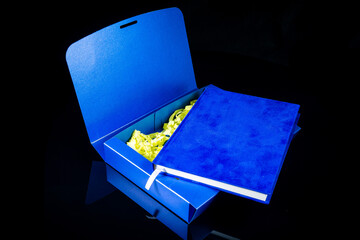 Best gift for men. Man gift concept. Blue notebook with blue gift box on black background. Copy space text. Valentine's day, wedding, birthday and special occasion gift concept. Copy space for text.