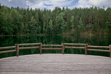 View of Chertok lake, calm lake, pine and spruce forest, clouds. Wooden viewpoint.