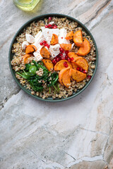 Quinoa with feta, roasted sweet potato, pomegranate and wilted spinach, top view on a light-grey granite background, vertical shot, copyspace
