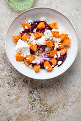 Plate of roasted sweet potato, feta cheese and radicchio salad, flat lay on a beige granite background, vertical shot with space