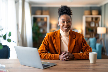 Smiling confident businesswoman looking at camera sitting at home office desk. Modern stylish female corporate employee successful executive manager with laptop posing for business portrait.