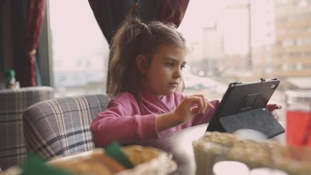 Child girl 6 years old in casual with tablet is sitting in cafe, digital education