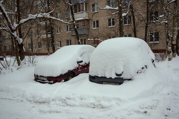 Cars covered completely by white heaps of snow in the street near houses