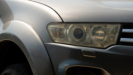 Headlights are old and dull of grey car. Car park in the parking area under sunlight.