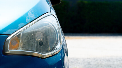 Headlights of bue car. with sunlight casting a radiant glow on the hood. The background depicts a...