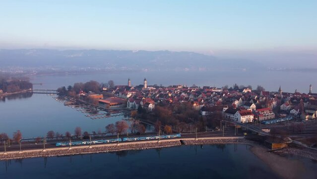 Winterstimmung am Bodensee, Inselstadt Lindau, Blick auf Bahndamm mit einfahrendem Zug, Eisenbahn, dahinter der See und die Berge mit blauem Himmel
