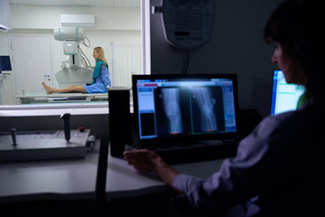 Experienced radiographer is performing digital lower limb radiography on patient - obrazy, fototapety, plakaty