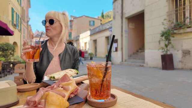 Tourist woman drinking a cocktail in the downtorn of Brisighella historic villgge in Italy, in emilia-romagna region. Aperitif based on Romagna piadina with raw ham and crescentine.