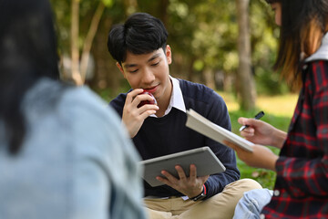 Close-up image of Young Asian man eating an apple while doing homework with his friends in the park