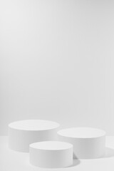 White abstract stage mockup with  three white round podiums for cosmetic products in hard light on white background. Scene for presentation cosmetic products, gifts, goods, advertising, design, sale.