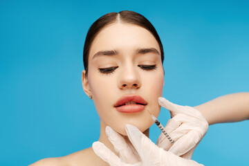 Young woman getting beauty injection in lips. Isolated on blue background. Beauty care, anti aging...