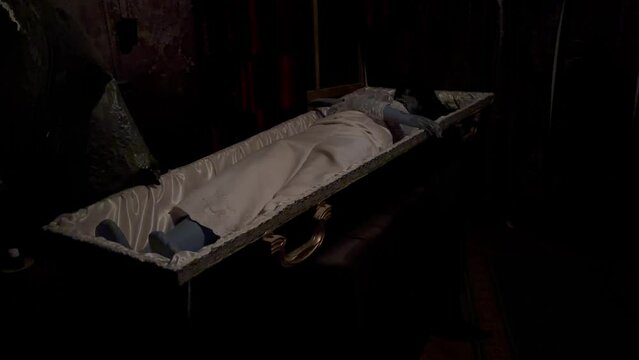 A coffin in a dark room of fear in which lies a dead witch mannequin with black hair and a white dress. The concept of death.