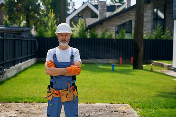 Tranquil builder in safety helmet standing on new building site