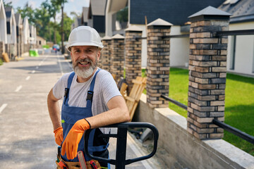 Cheerful building contractor posing for camera among houses under construction