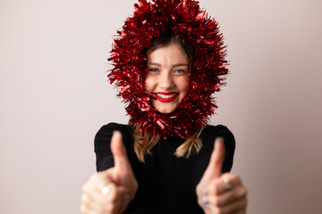 Young blonde woman with red garland decoration over her head showing thumbs up.