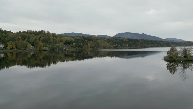 Ascending aerial footage over the peaceful and placid waters of Staffelsee, reflecting trees and scenery against the backdrop of the German Alps