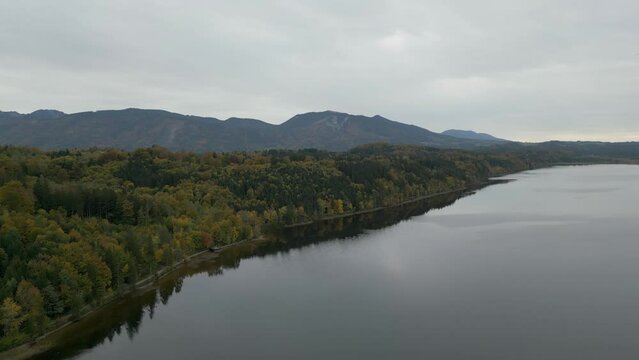 Panning aerial footage of the peaceful and placid waters of Staffelsee, reflecting trees and scenery against the amazing backdrop of the German Alps