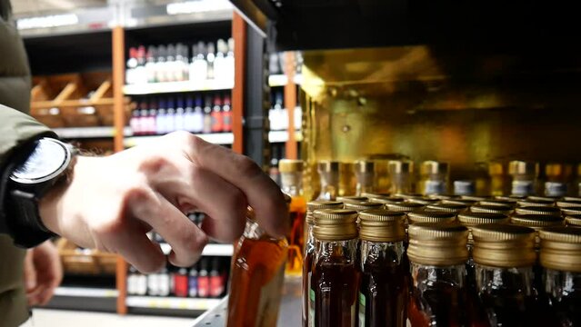 Close-up of many beautiful small bottles of cognac rum or brandy in a liquor store and a male buyer comes up and takes one