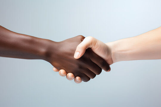 saludo interracial de una mano de persona de color y otra blanca, realizando un apret&oacute;n de manos a modo de saludo o acuerdo
