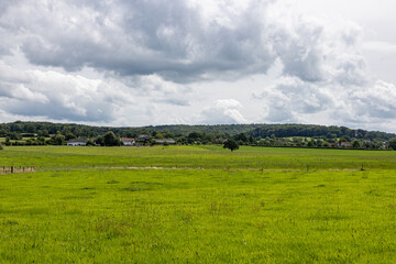 Dutch agricultural plain with grassland in Dutch agricultural landscape, farm, leafy trees covering hill against cloud covered sky in background, sunny day in Epen, South Limburg, Netherlands