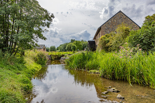 River Geul with old Eper watermill or Wingbergermolen in background, surrounded by wild vegetation and trees against cloud-covered sky, cloudy day at Terpoorterweg, Epen, South Limburg, Netherlands