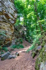 Hiking trail on a hill, rocky slope or wall of an eroded rock formation and sunlit green trees in background, sunny day in Teufelsschlucht nature reserve, Irrel, Germany