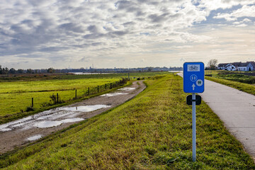 Bike path in Belgian nature reserve De Wissen, between a hiking trail with puddles and countryside, farms in background, routes 50 and 19, cloudy day with cloud-covered sky in Dilsen-Stokkem, Belgium