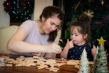 Mother and young daughter sit together and decorate Christmas cookies with icing