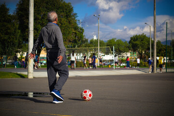 Happy retired senior man kicking a ball playing soccer in a park outside in the afternoon