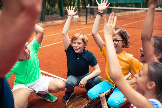 Happy children raising hands during tennis practice