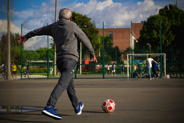 Happy retired senior man kicking a ball playing soccer in a park outside in the afternoon