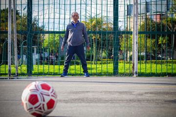 Retired older man being a goalkeeper on a soccer field in a park