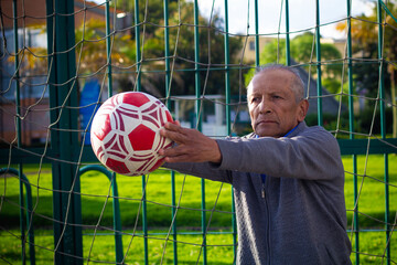 Retired older man being a goalkeeper on a soccer field in a park