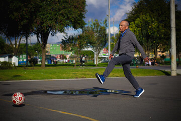 Happy retired senior man kicking a ball playing soccer in a park outside in the afternoon
