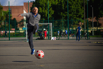 Happy retired senior man kicking a ball playing soccer in a park outside in the afternoon