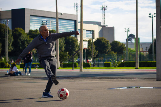 Happy retired senior man kicking a ball playing soccer in a park outside in the afternoon - Powered by Adobe