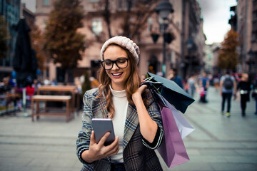 Young stylish woman using smartphone while shopping in city - obrazy, fototapety, plakaty