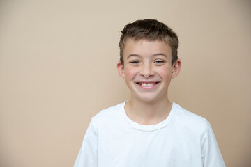 cool 11 years old boy with white t-shirt  in front of brown background in the studio - obrazy, fototapety, plakaty