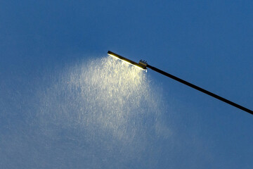 A street lamp in selective focus shines in a snowfall, blizzard, storm on a winter night.Picture...