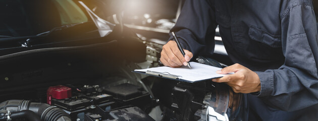 Auto check up and car service shop concept. Mechanic writing job checklist to clipboard to estimate...