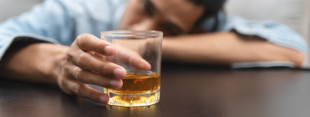 melancholy young Asian man drinks alcoholic whisky alone at home feeling dizzy after drunk