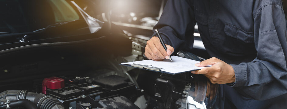 Auto check up and car service shop concept. Mechanic writing job checklist to clipboard to estimate repair quotation to client at workshop garage.