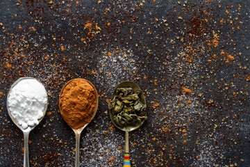 Spoons with icing sugar, green tea and cocoa on black background sprinkled with sugar, coffee,...