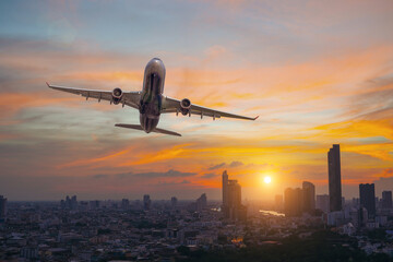 Commercial airplane flying over city with skyscrapers at evening sunset golden hour.
