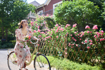 Young and beautiful women ride bicycles in the courtyard full of flowers