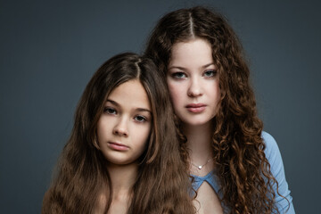 Obraz premium Studio portrait of two beautiful sisters in blue shirts and jeans against gray background.