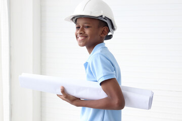 Happy smiling African boy wearing helmet safety hard hat, holding blueprint, standing on white wall...